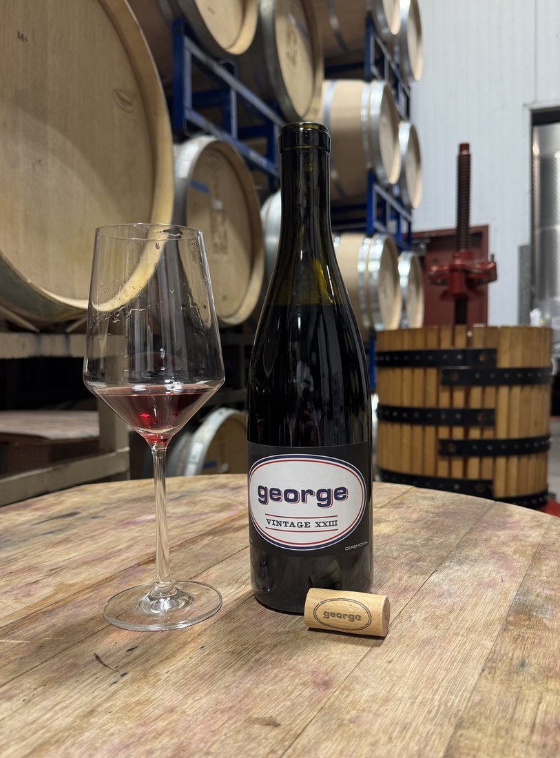 A bottle of George Pinot Noir with a glass in the barrel room